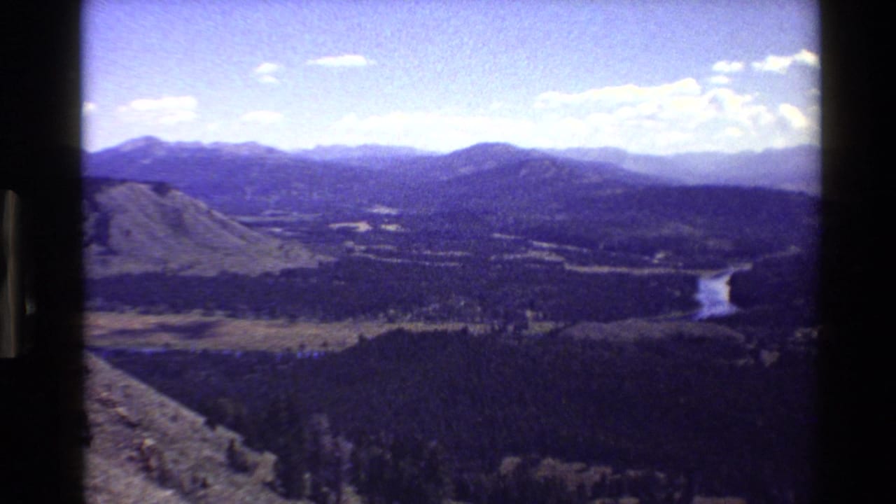 High view over a forested mountain valley with a winding river and distant ridges.