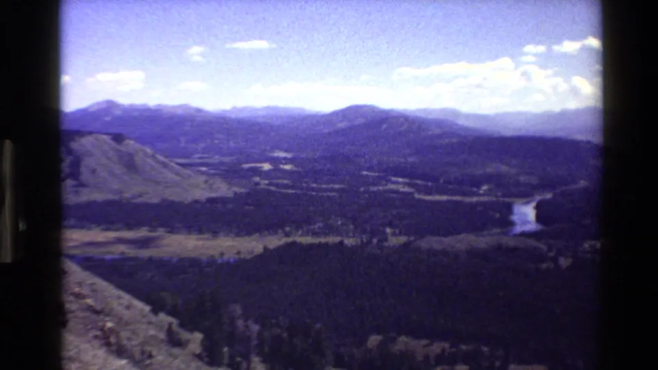 1980 Grand Teton view from a high vantage point, showing a winding river, forested valley, mountains, and bright sky.