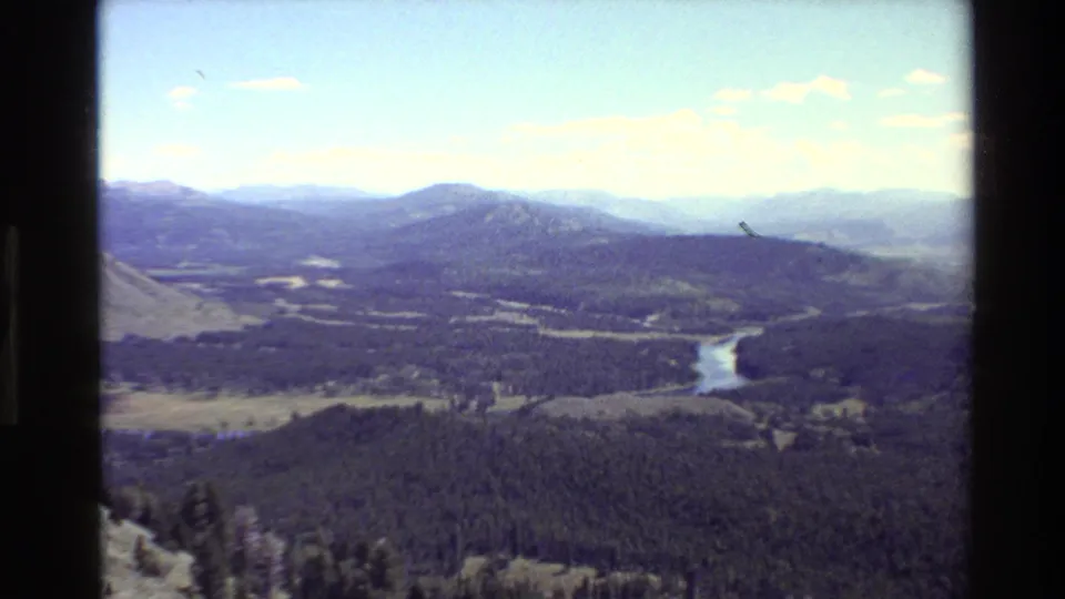 Wide 1980 Grand Teton panorama showing forested valley, open meadows, a curving river, and hazy mountain ridges.
