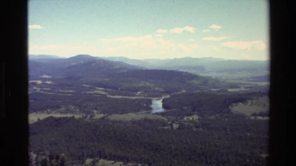 Grand Teton, Wyoming landscape from 1980 8mm footage, with forest, river, distant mountains, and pale sky.