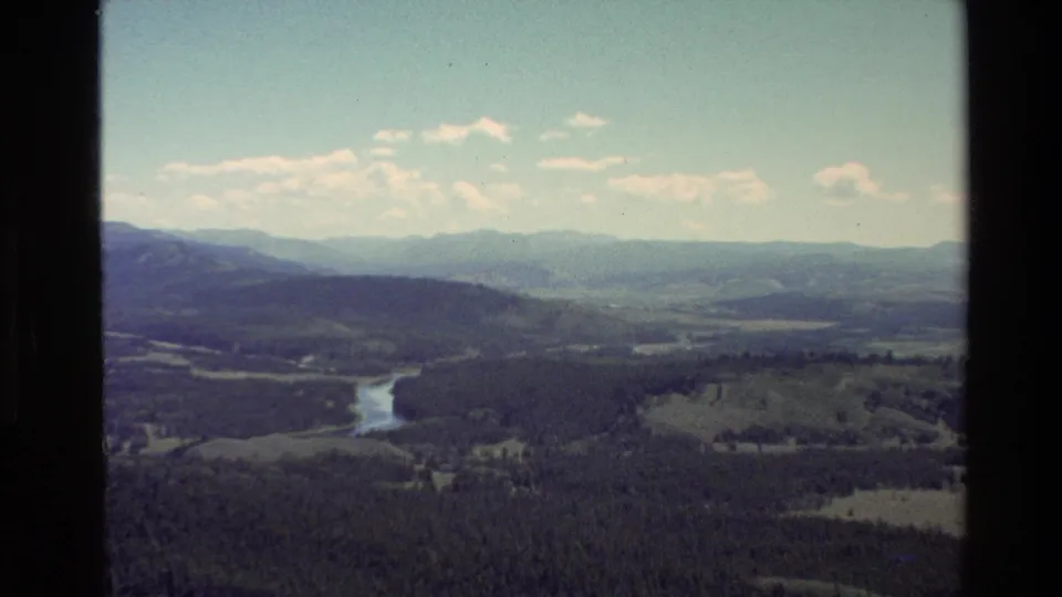 Grand Teton-area 8mm travel footage from 1980 shows a river winding between forested slopes and fields beneath hazy mountain ridges.