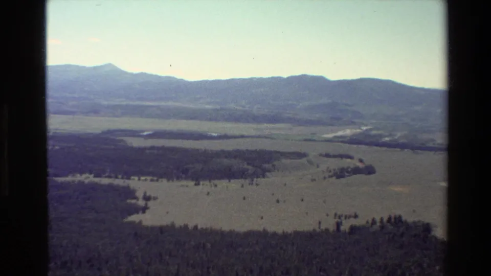 Grand Teton, Wyoming 8mm frame showing a distant mountain ridge over forested valley, open land, and small water features from a hilltop view.