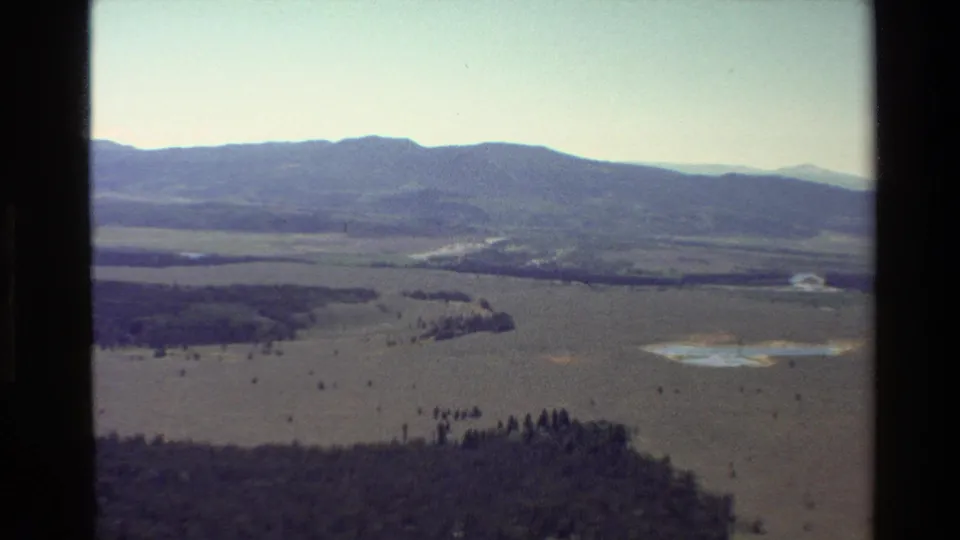Grand Teton, Wyoming 8mm frame from 1980 with a high view across plains, forested areas, water, and hazy mountain ridges.