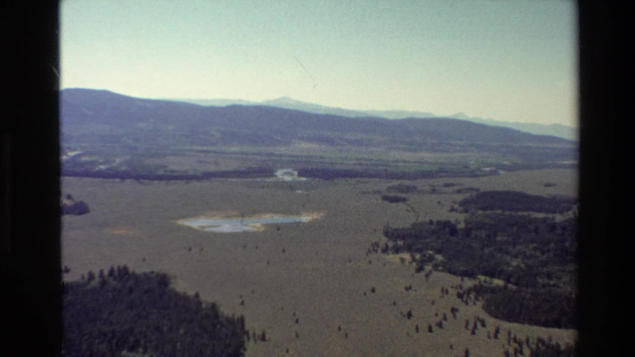 Aerial view of a mountain valley with scattered trees, small water areas, and dark window framing.