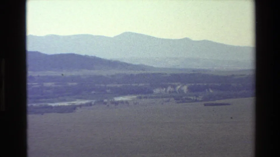 Grand Teton-area landscape with distant blue ridges, open fields, and a winding river or watercourse below.