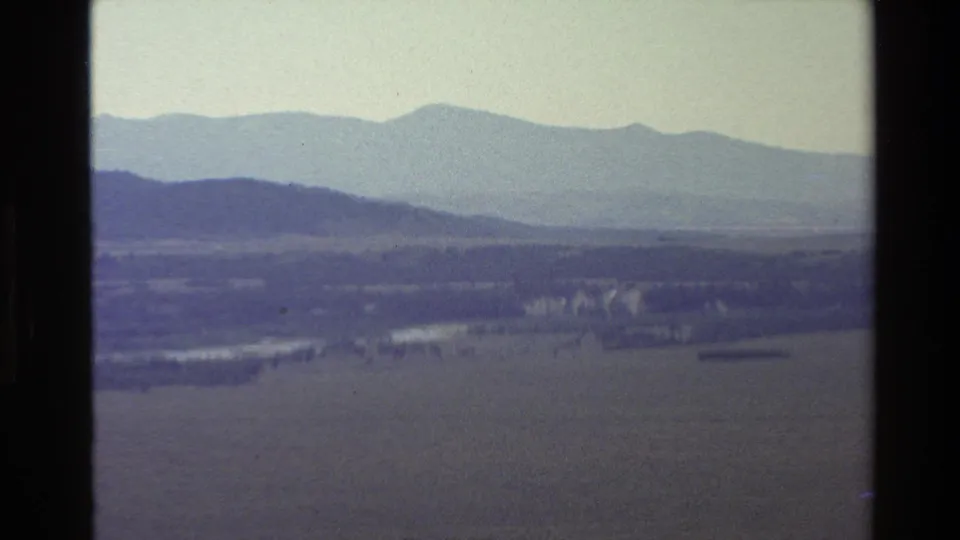 1980 8mm scenic view in the Grand Teton area, showing mountains over fields and a faint watercourse.