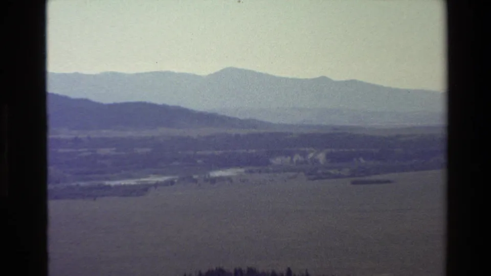 Grand Teton-area home-movie frame of hazy mountains, valley fields, and a winding river or watercourse.