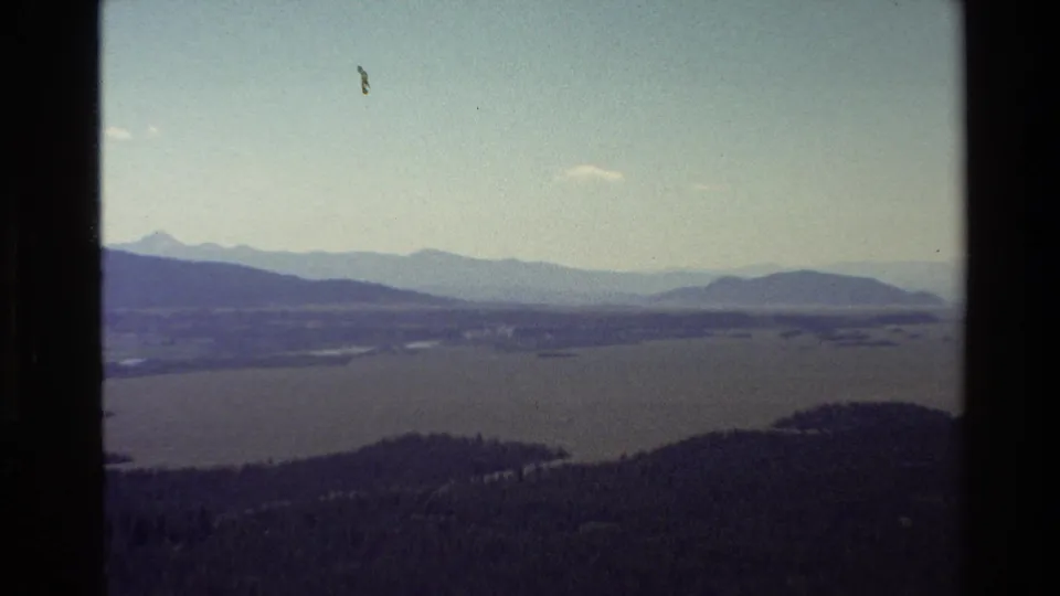 Grand Teton-area lake and mountain panorama, filmed on 8mm with soft color and dark vertical framing at the edge.