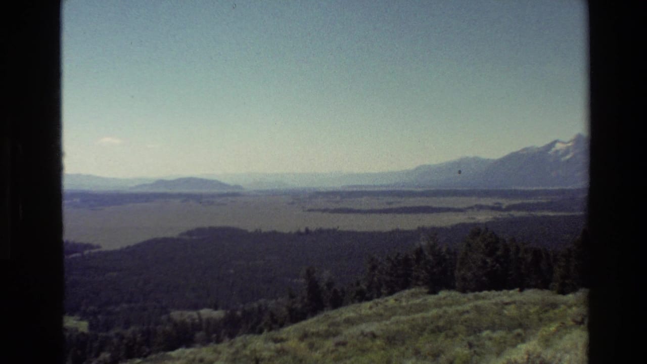Wide mountain and lake view with forested ridges and grassy foreground.