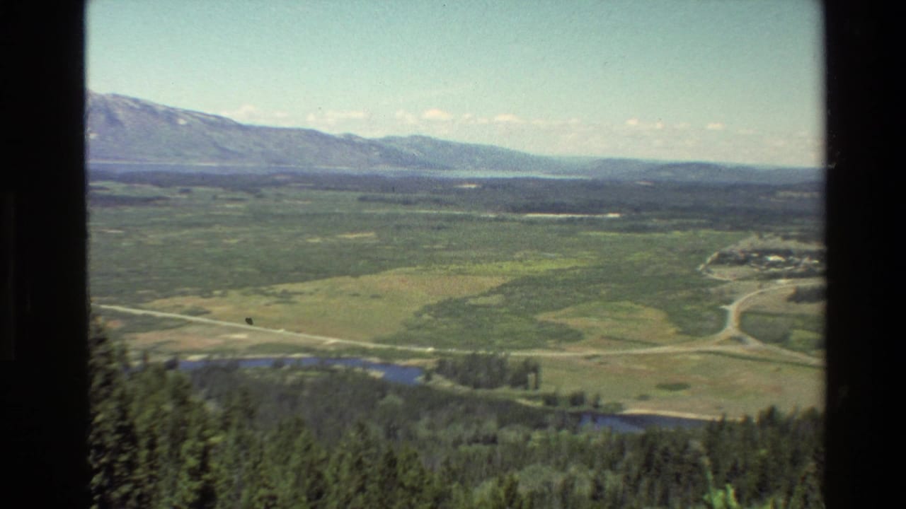Elevated valley view with mountains, forest, water, roads, and dark frame borders.