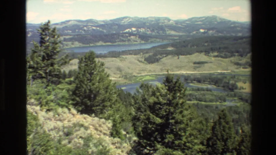 Final 1980 8mm Grand Teton frame showing a high scenic overlook across evergreens, valley water, forests, and mountain ridges.