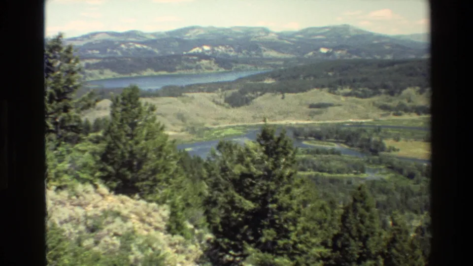 1980 Grand Teton, Wyoming 8mm frame showing a green valley, winding river, lake, pine trees, and distant snow-patched mountains.