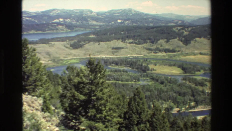 1980 Grand Teton, Wyoming 8mm view across a wooded slope, winding river valley, lake, and distant mountains.