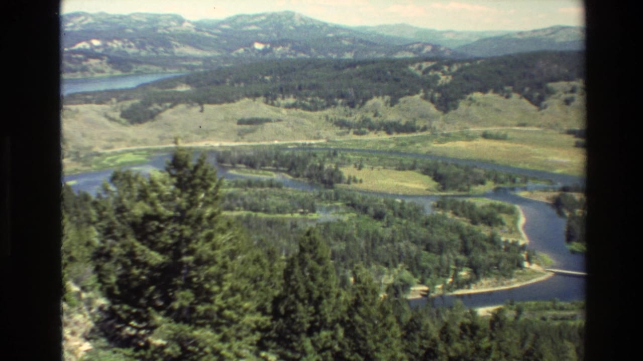 Winding river through forest and meadow with distant mountains and dark film borders.