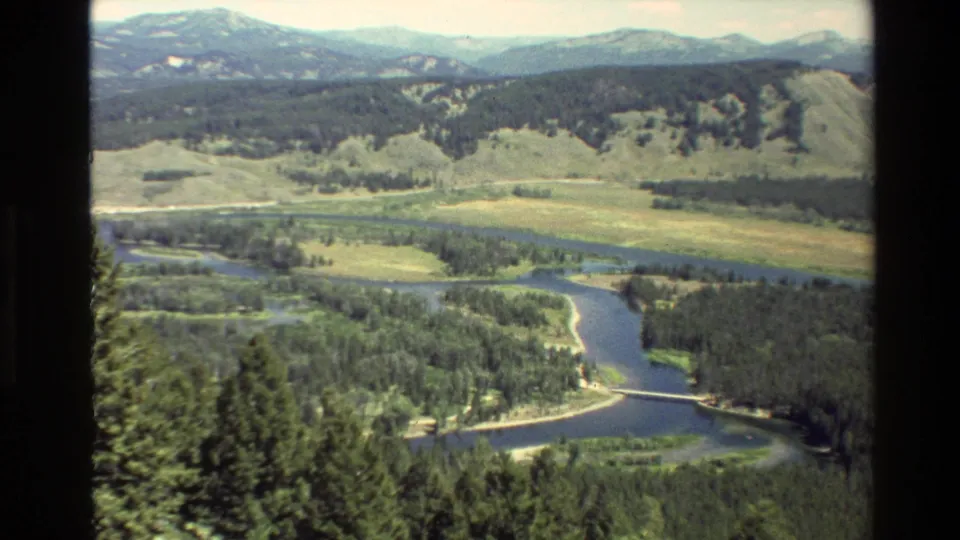 Grand Teton landscape in 8mm color, showing a river corridor through forest and meadow with hills and distant mountain ridges.