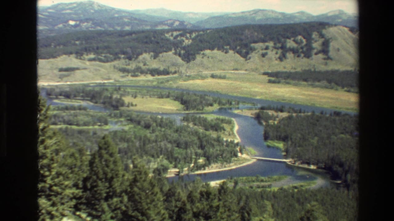 1980 Grand Teton, Wyoming 8mm frame showing a river or lake channel, dense trees, open valley, and distant mountain ridges.
