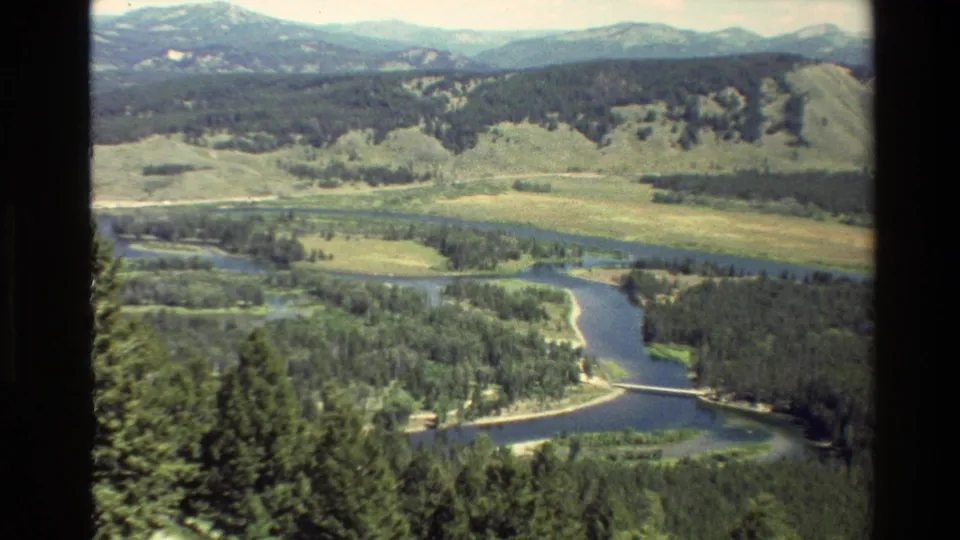 1980 Grand Teton, Wyoming 8mm frame showing a river or lake channel, dense trees, open valley, and distant mountain ridges.