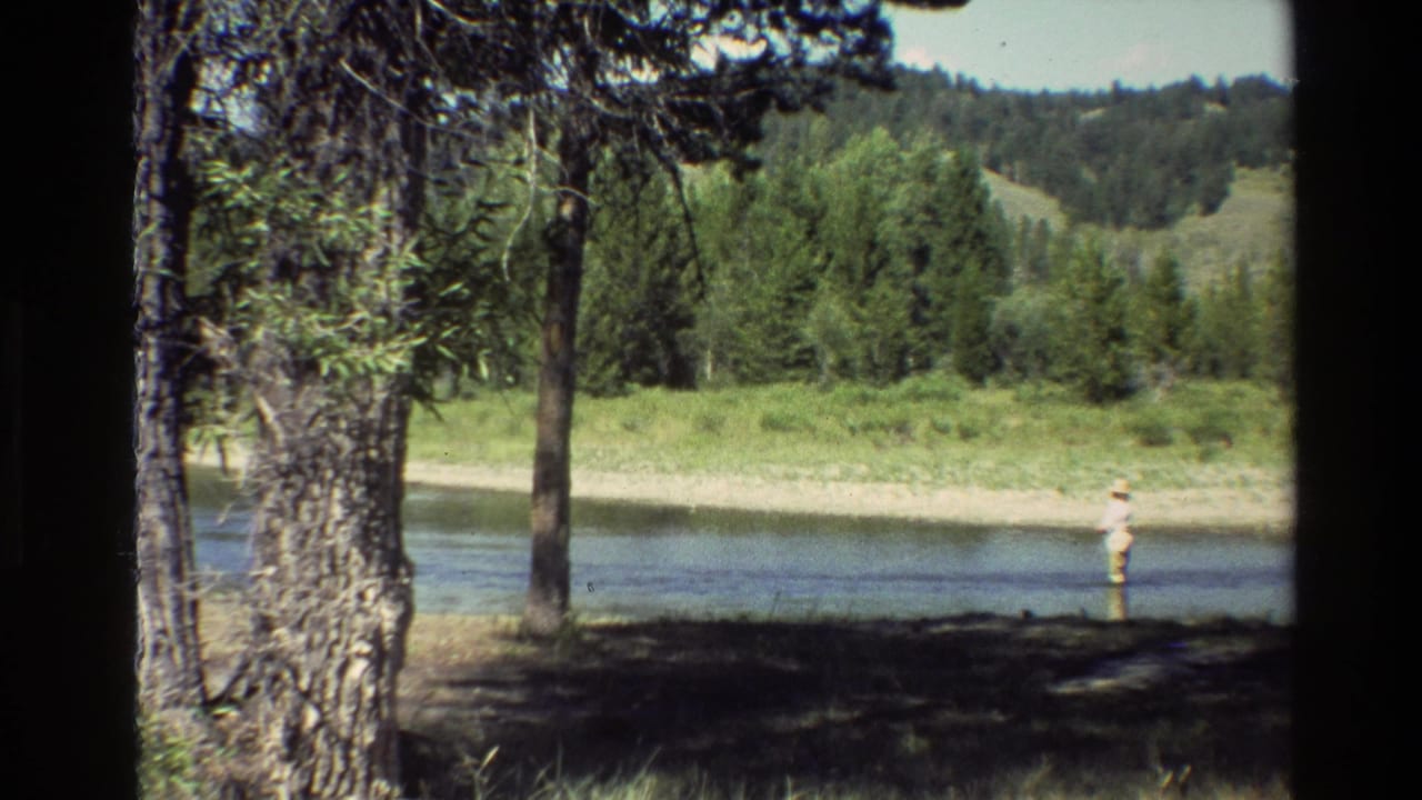 Grand Teton, Wyoming 1980 home-movie frame with a distant angler standing in a river near trees and low wooded hills.