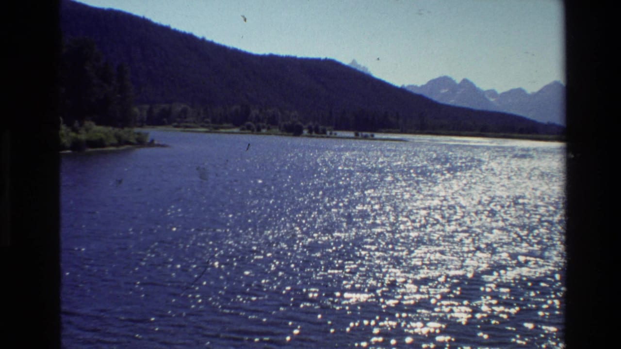 Sparkling lake with wooded shore and mountains in the distance.