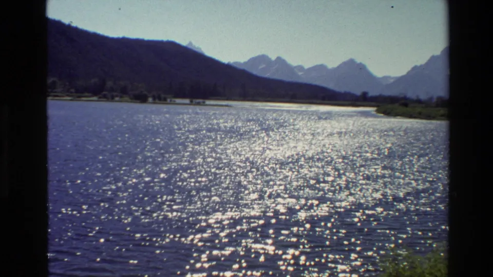 8mm Grand Teton landscape frame with rippled lake water in the foreground, a wooded shore, and the Teton range visible in the distance.