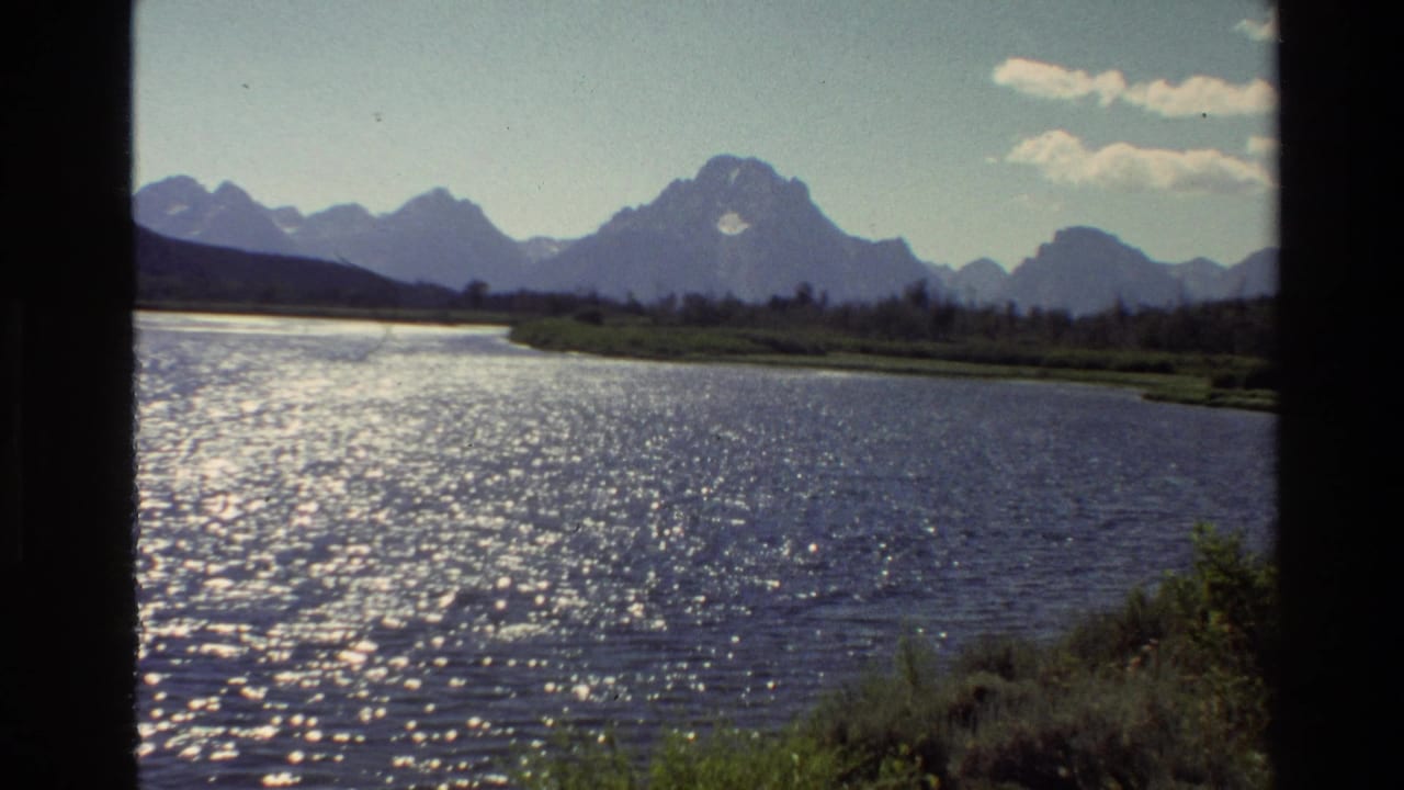 1980 8mm view of Grand Teton, Wyoming, with bright reflections on calm water and mountains across the horizon.