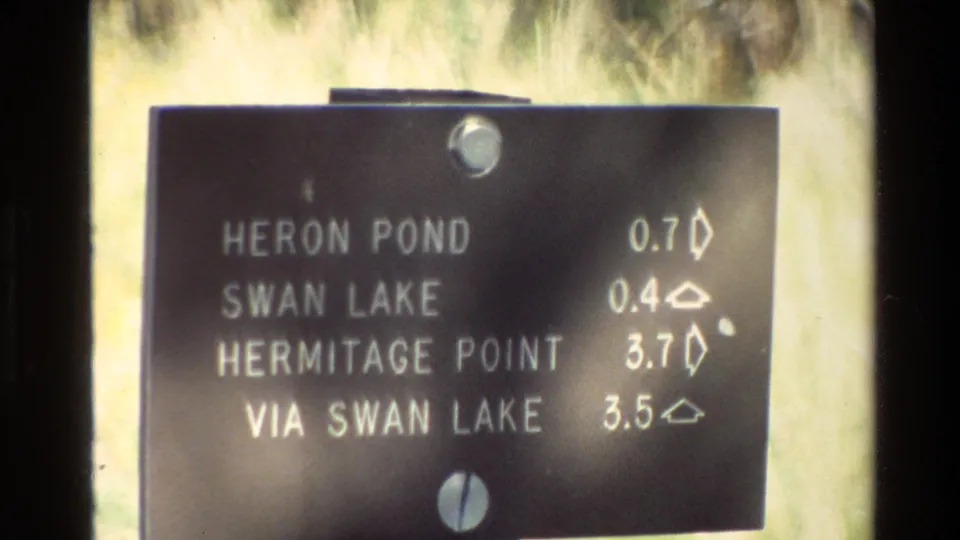 Grand Teton visitor footage from 1980 holds on the directional sign for Heron Pond, Swan Lake, Hermitage Point, and Via Swan Lake.