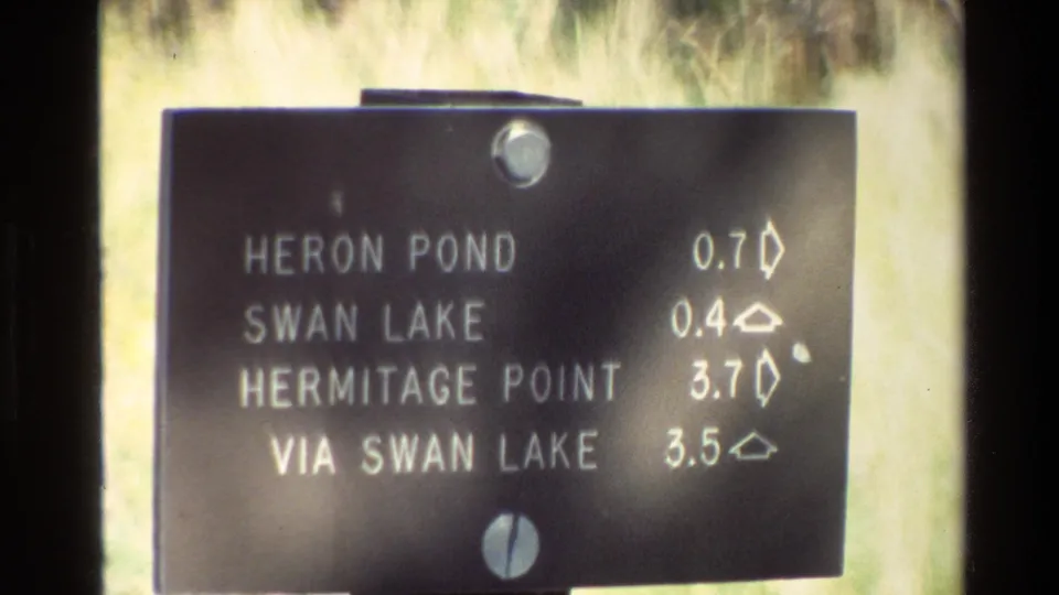 Soft 8mm frame of a Grand Teton directional sign showing distances to nearby lake and trail destinations in 1980 visitor footage.