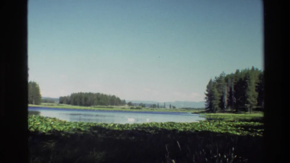 Grand Teton, Wyoming lake scene on 8mm film, framed by a window with trees at both sides and hazy mountains beyond.