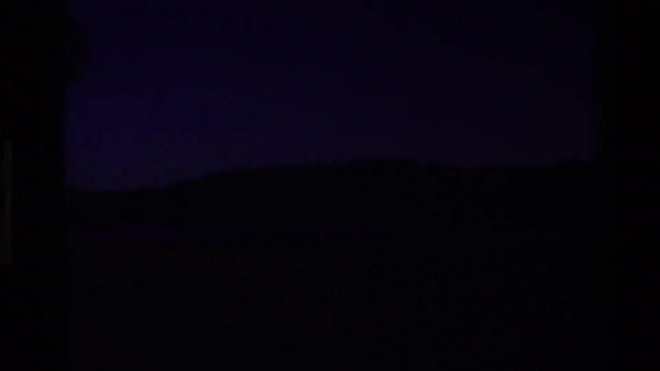 Dark, underexposed or damaged 8mm frame with faint landscape silhouettes visible near the horizon.