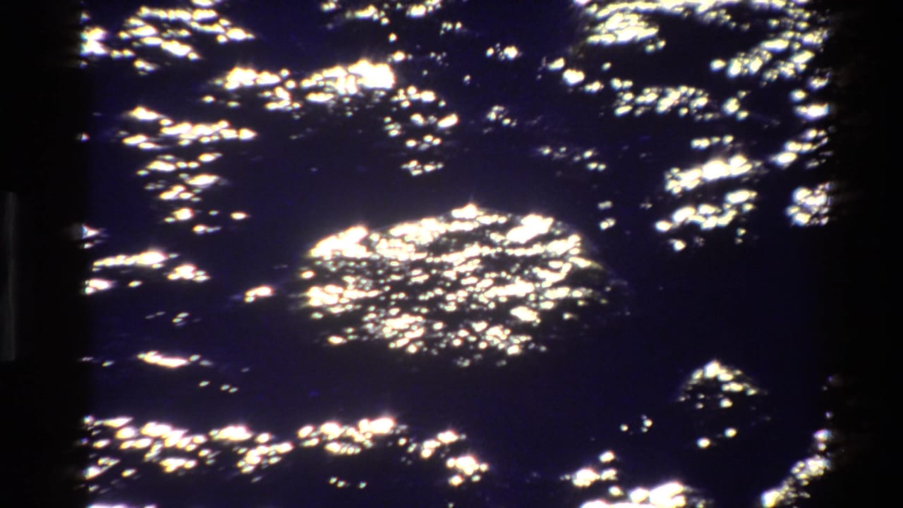 Abstract 8mm frame of sun glints scattered across dark lake water in the Grand Teton travel footage.