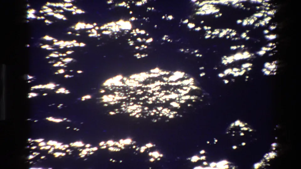Abstract 8mm frame of sun glints scattered across dark lake water in the Grand Teton travel footage.