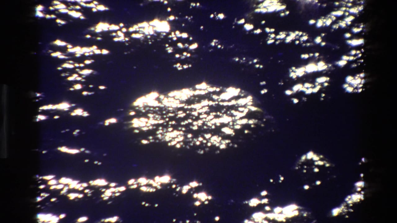 Dark lake surface with bright shimmering reflections and a shadowed vertical film edge.