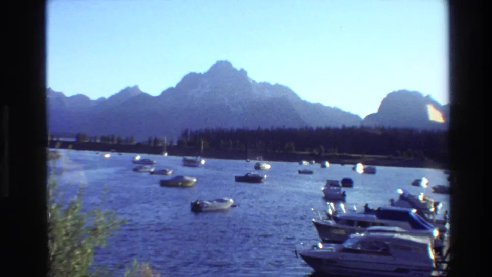 Wide Grand Teton, Wyoming lake view with boats on the water, a forested shoreline, and mountains in the background.