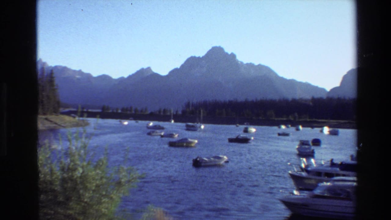 1980 8mm view of boats on a Grand Teton lake, with evergreen shoreline and mountain peaks beyond the water.