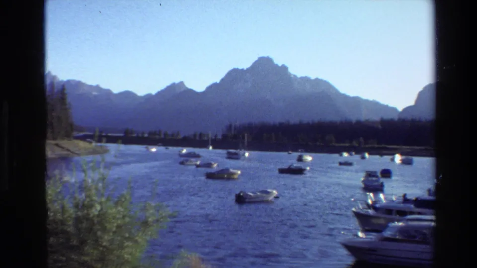 1980 8mm view of boats on a Grand Teton lake, with evergreen shoreline and mountain peaks beyond the water.