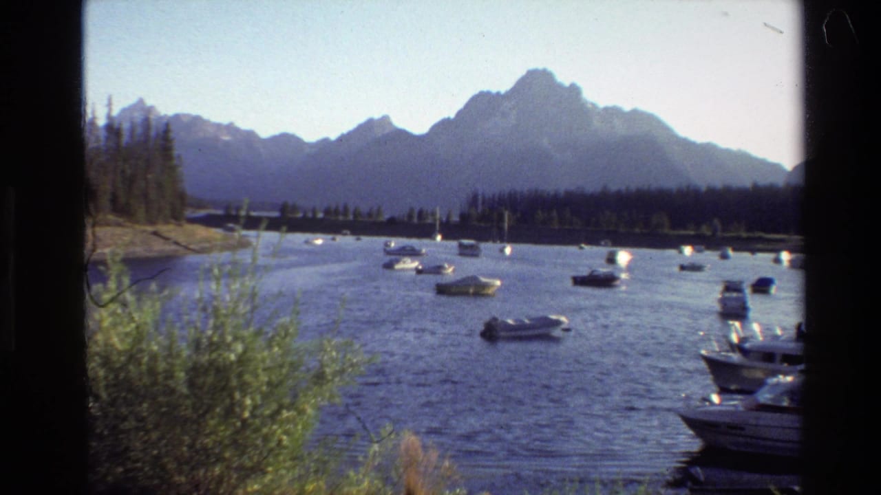Small boats floating on a lake with dark mountains and trees in the background.