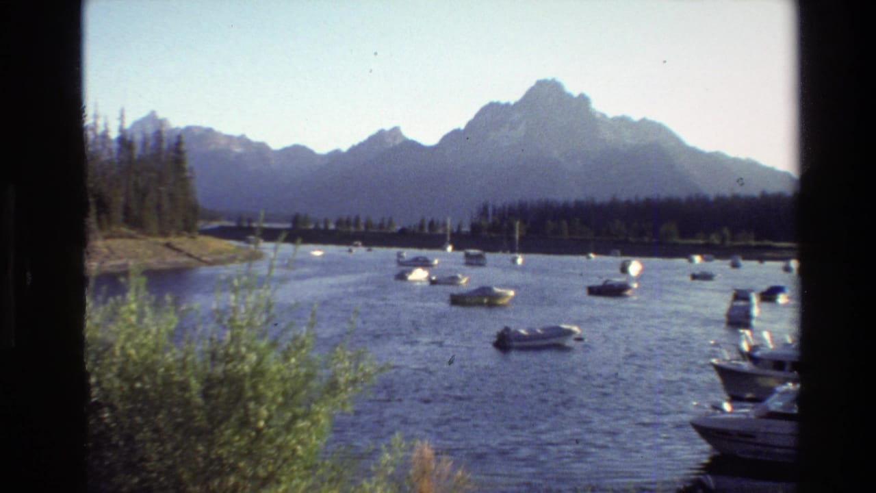 Grand Teton, Wyoming lake scene from 1980 8mm footage, showing anchored boats, calm water, trees, and distant peaks.