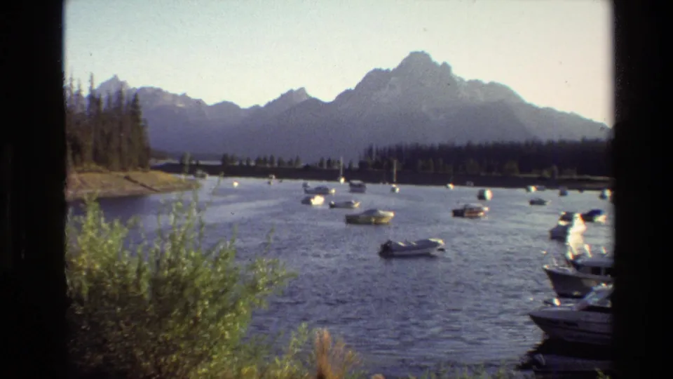 1980 Grand Teton home-movie frame showing boats on a lake with trees and the Teton Range beyond.