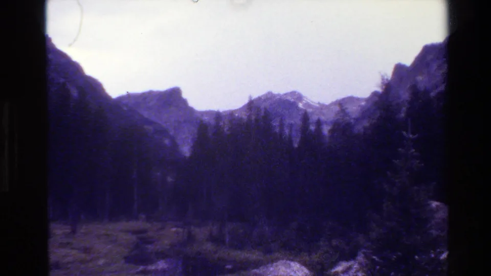 1980 Grand Teton, Wyoming landscape frame showing evergreen trees, rugged peaks, meadow, and pale sky with visible film borders.