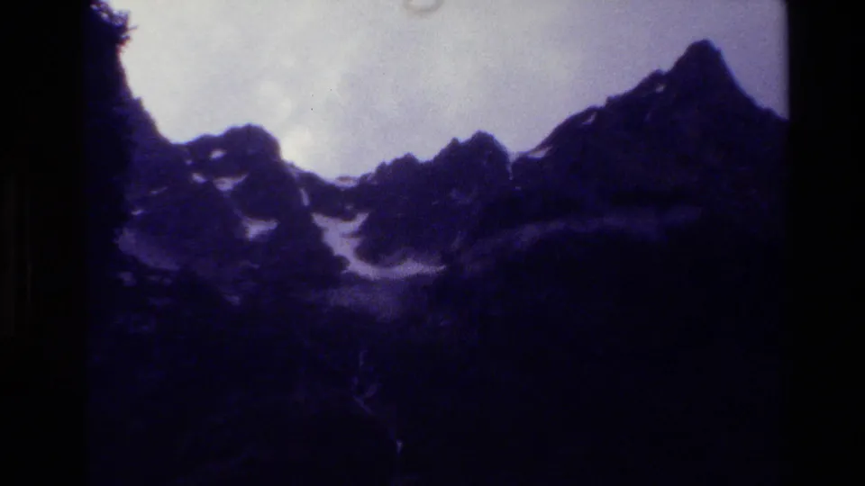 Grand Teton mountain view in purple-tinted 8mm footage, showing dark ridges, snow patches, and an overexposed sky.
