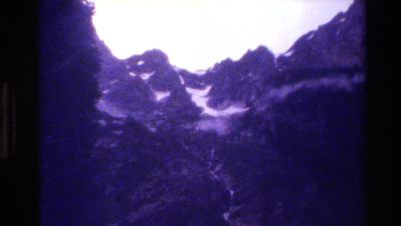 Grand Teton landscape frame with snow patches on steep peaks and a shadowed forest valley beneath.
