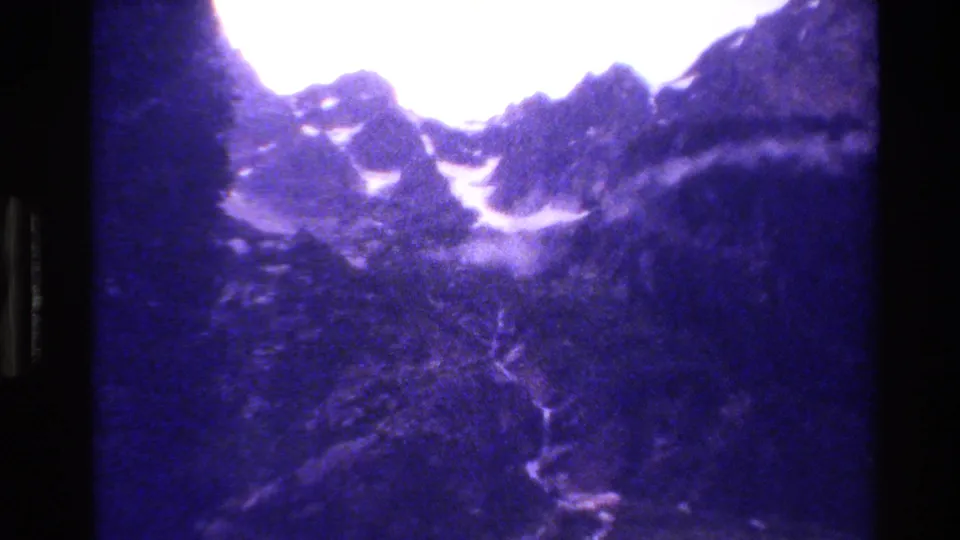 1980 Wyoming mountain view with snowy peaks, dense dark slopes, and a pale line running through the valley floor.