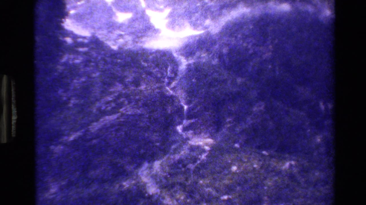 1980 Grand Teton 8mm frame showing a rocky canyon wall and bright mountain waterfall under heavy purple color shift.