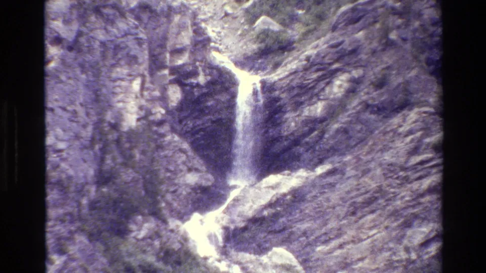 1980 Wyoming 8mm frame showing a mountain waterfall descending into lighter rocks at the canyon base.