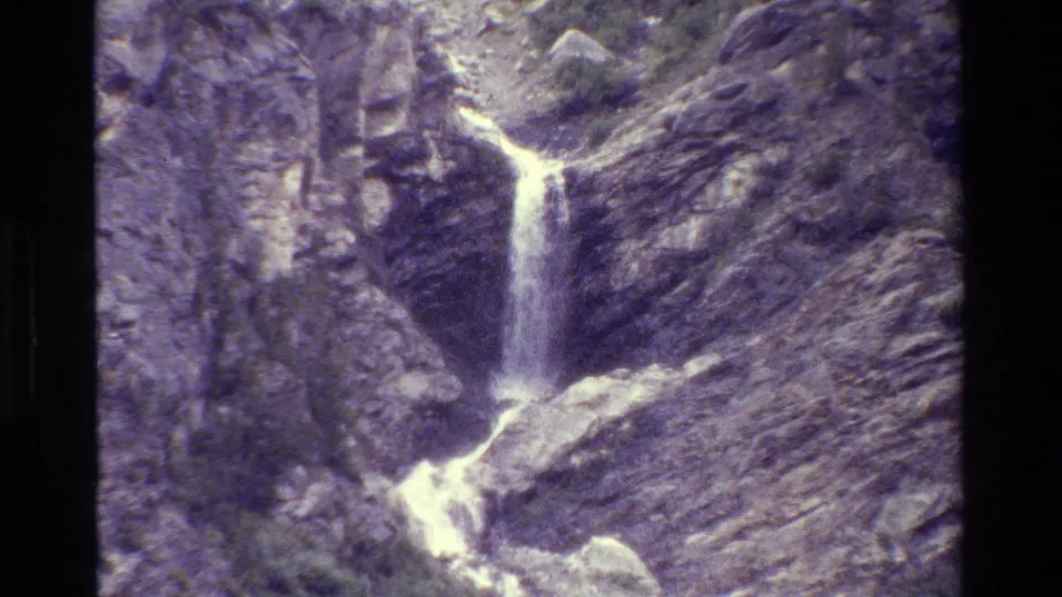 Grand Teton 1980 home-movie frame with a narrow white cascade running down a steep rocky canyon wall.