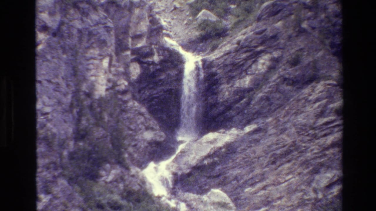 1980 8mm Grand Teton footage showing a small waterfall dropping through gray rock in bright outdoor light.