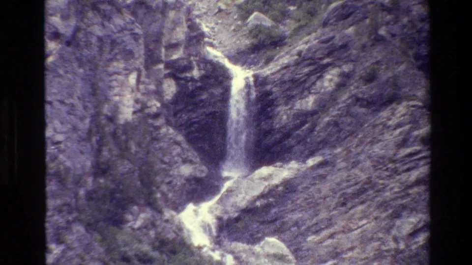 1980 8mm Grand Teton footage showing a small waterfall dropping through gray rock in bright outdoor light.