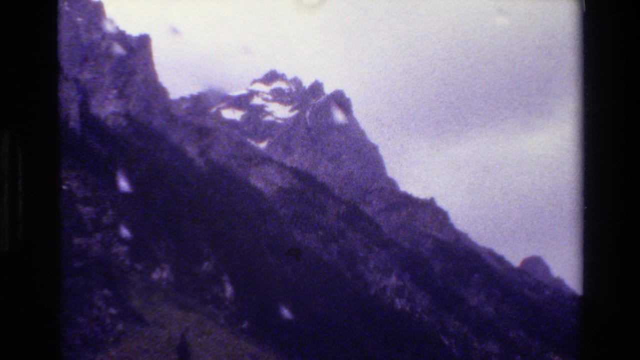 Rugged mountain ridge with patches of snow beneath a pale cloudy sky.