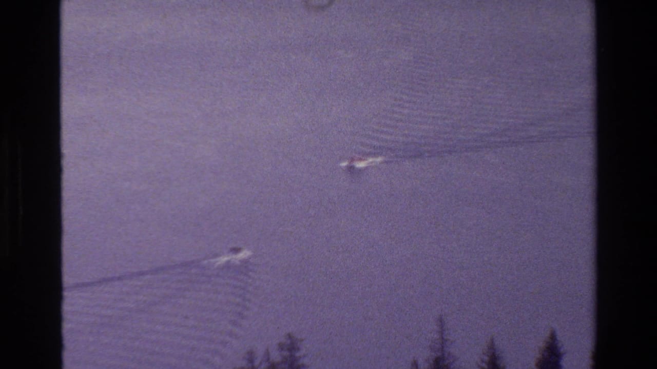 Grand Teton, Wyoming 1980 home-movie frame showing two small boats crossing calm lake water near an evergreen shoreline.