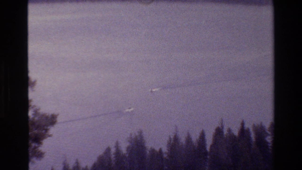 Grand Teton, Wyoming 1980 lake view with small boats and wakes above a dark evergreen shoreline in 8mm film framing.